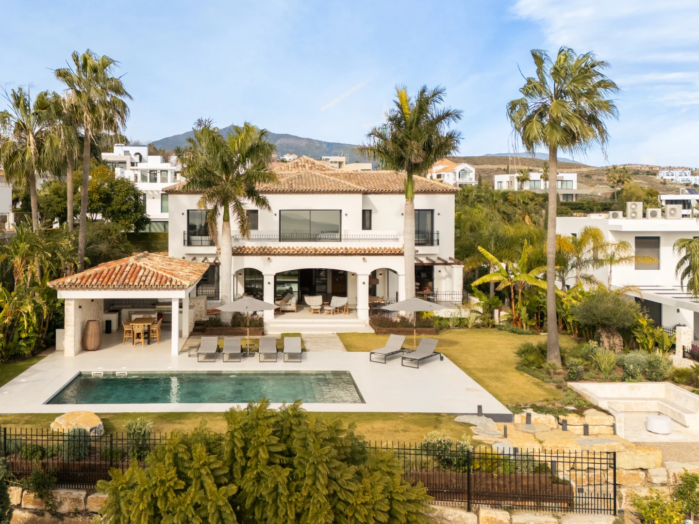 White Andalusian villa with terracotta roof, arched loggia, pool and gardens below the mountains